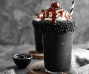 Creamy black milkshake topped with whipped cream and chocolate syrup in a tall glass, perfect for a decadent dessert treat.