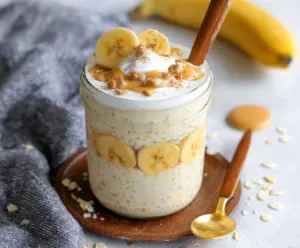Delicious Banana Cream Pie Protein Overnight Oats in a glass jar with bananas and whipped cream topping