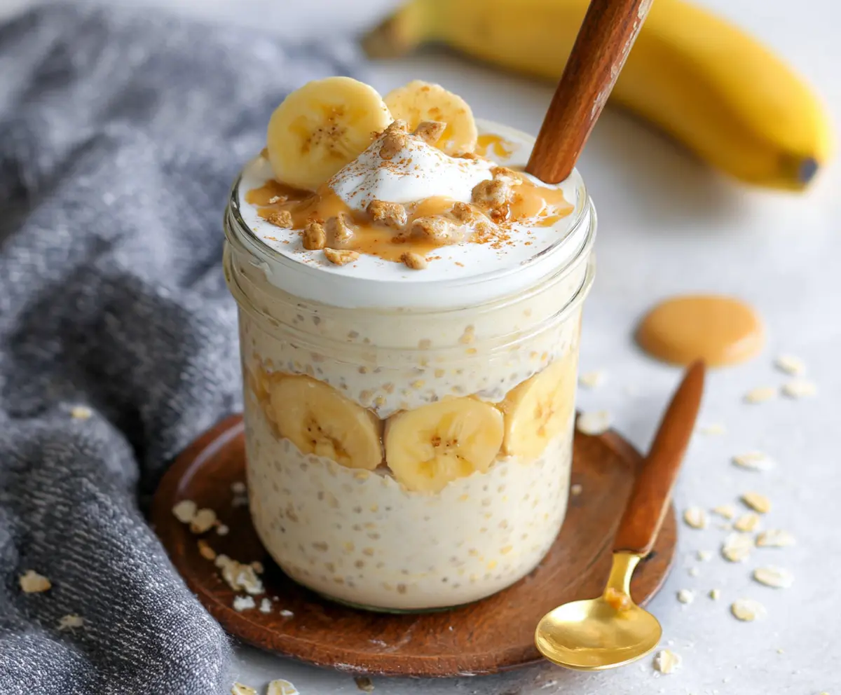 Delicious Banana Cream Pie Protein Overnight Oats in a glass jar with bananas and whipped cream topping