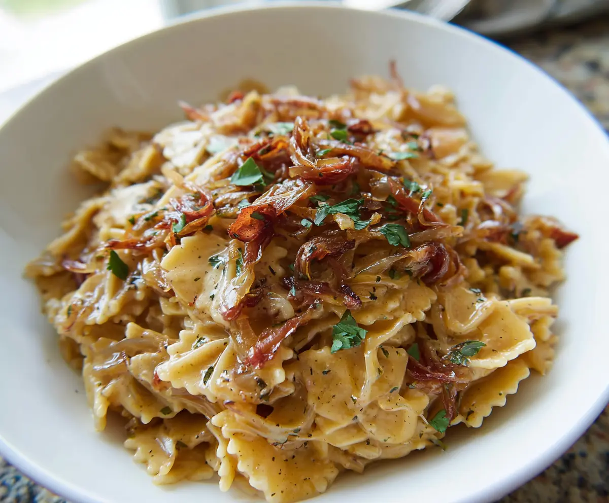 Delicious caramelized onion pasta served on a plate, showcasing golden-brown onions and pasta garnished with herbs.