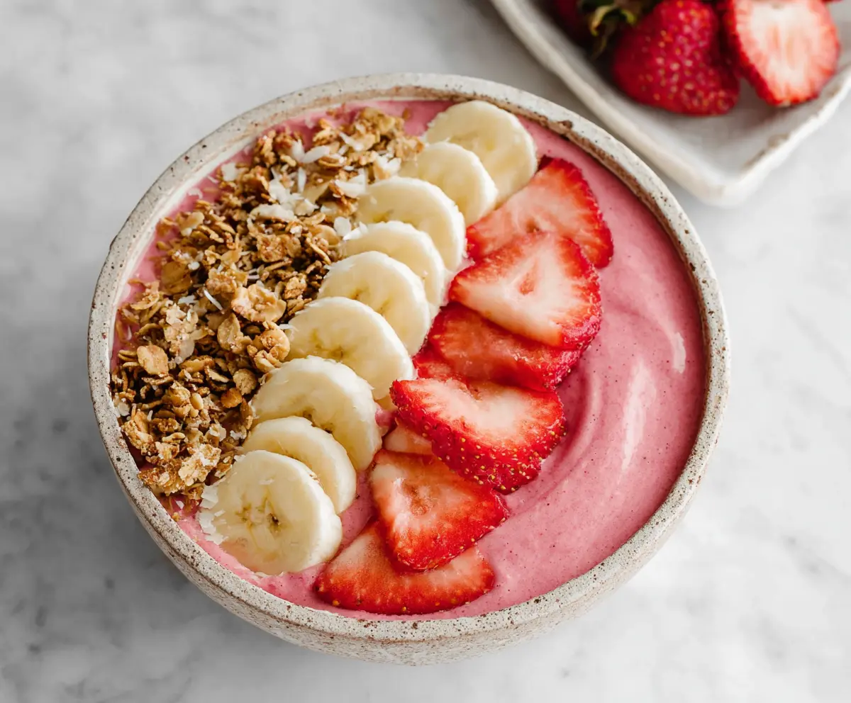 Colorful strawberry and banana smoothie bowl topped with fresh fruit and granola.