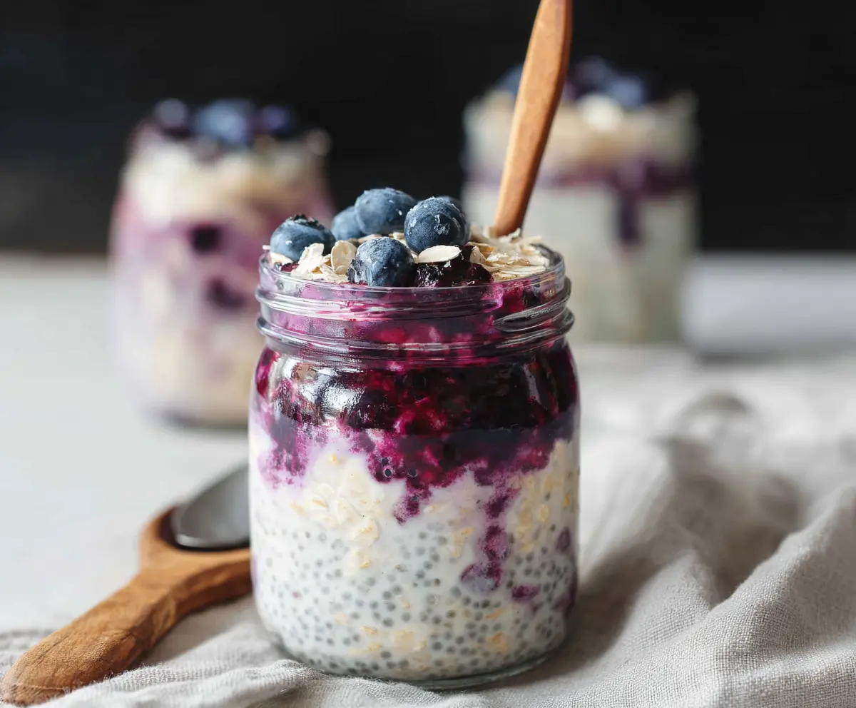 Creamy blueberry cheesecake overnight oats in a glass jar topped with blueberries and a sprig of mint.
