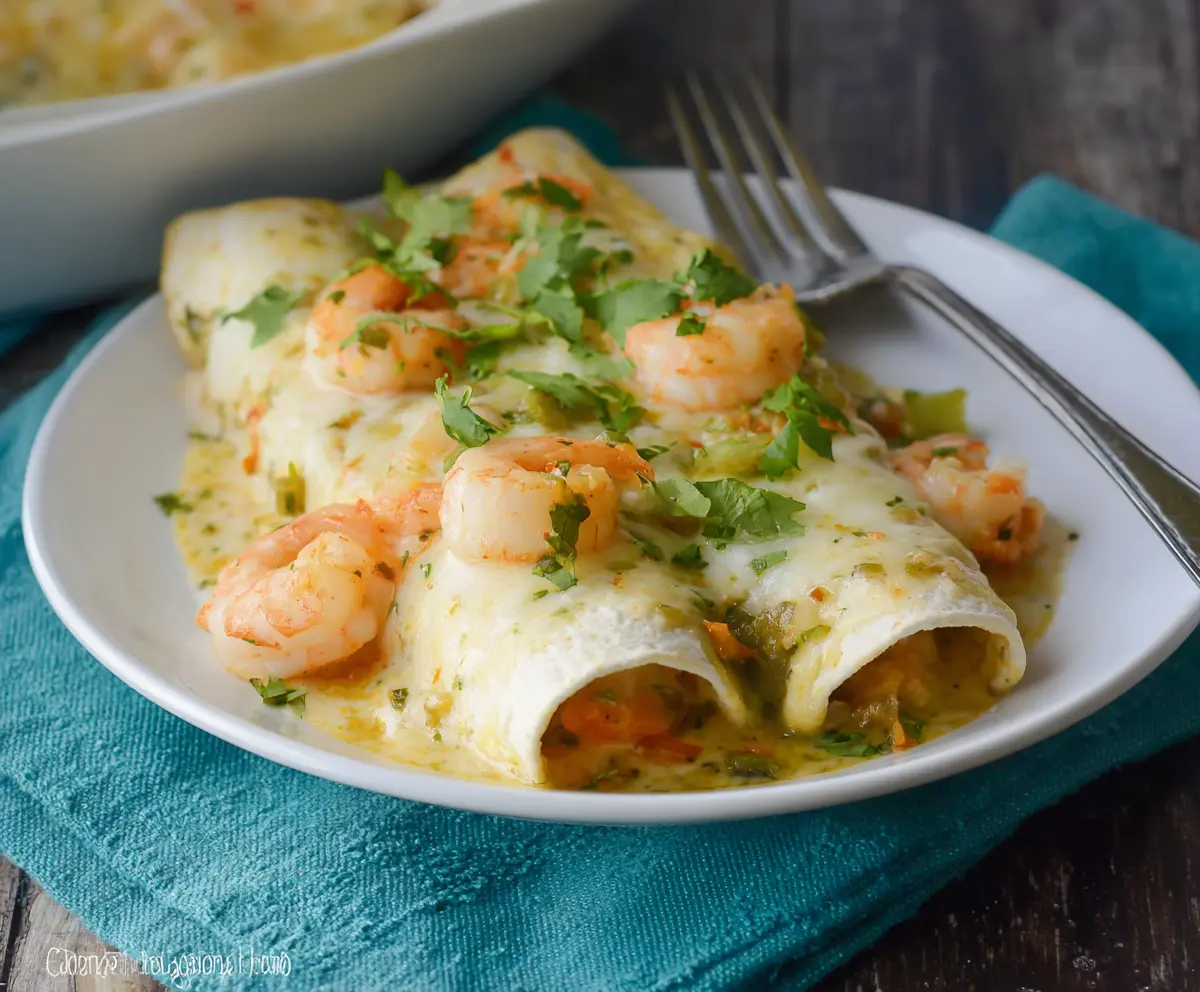 Delicious creamy shrimp enchiladas with melted cheese and fresh herbs on a plate.