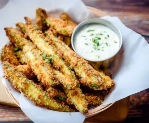 Crispy pickle fries served with dipping sauce on a wooden platter, perfect for snack or appetizer.