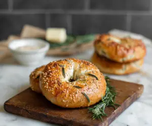 Freshly baked rosemary bagels on a baking tray, garnished with sprigs of rosemary.