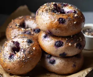 Freshly baked sourdough blueberry bagels on a wooden surface with blueberries.