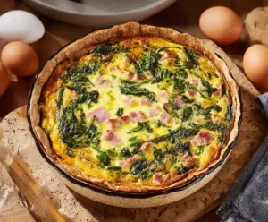 Delicious Easter ham and spinach quiche served sliced on a white plate, topped with fresh herbs.