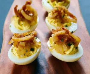 Delicious French Onion Deviled Eggs garnished with herbs on a white plate.