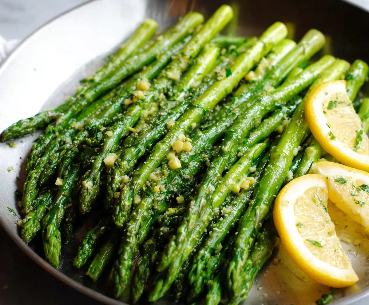 Fresh lemon garlic asparagus on a white plate, garnished with herbs for a vibrant, healthy side dish.